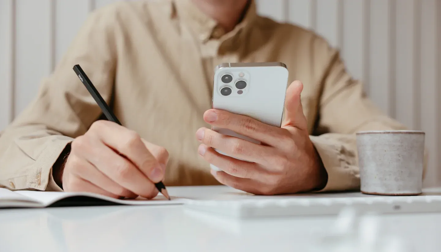 man holding mobile phone while filling in paperwork